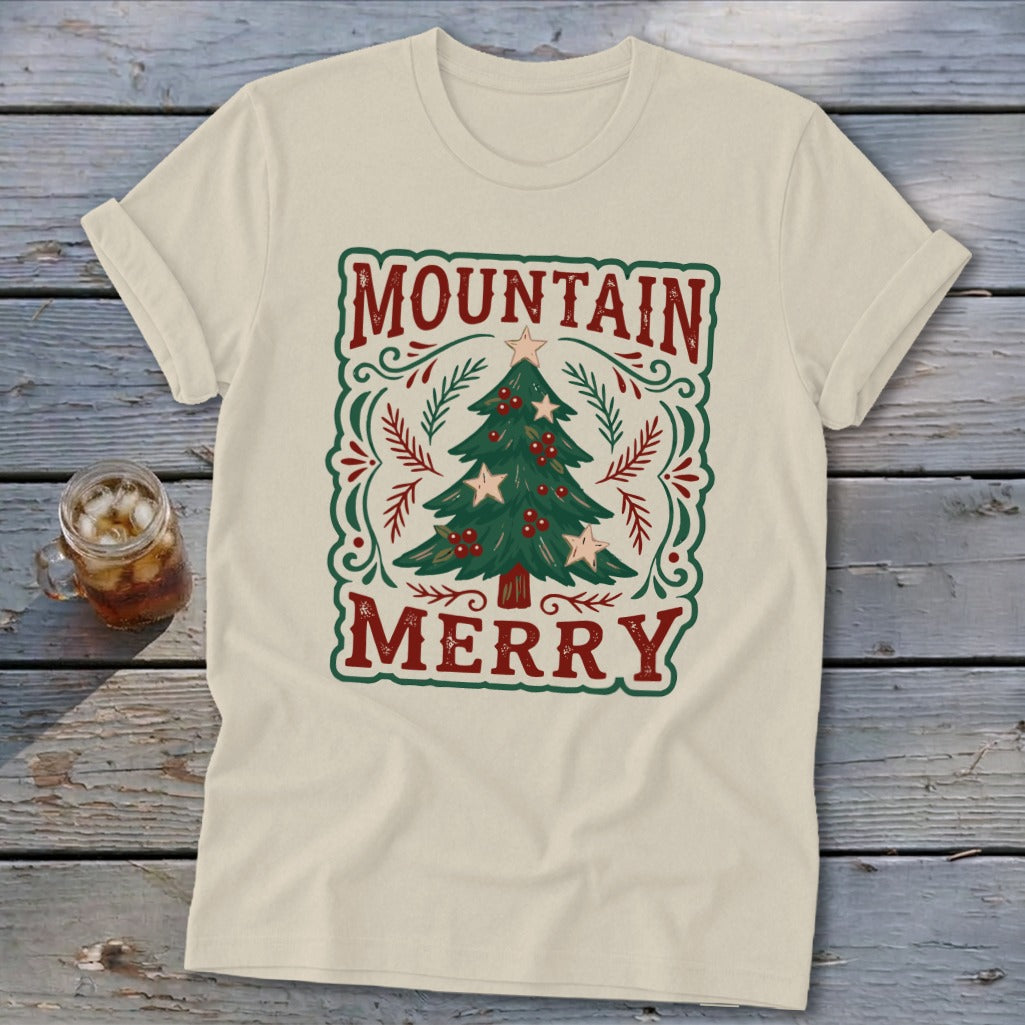 Beige t-shirt featuring a green Christmas tree graphic, red berries, stars, and the text MOUNTAIN MERRY.
