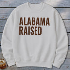 White sweatshirt with "ALABAMA RAISED" printed in brown text.
