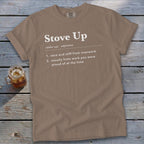 A brown t-shirt featuring dictionary-style text defining the phrase Stove Up, displayed on a wooden background.