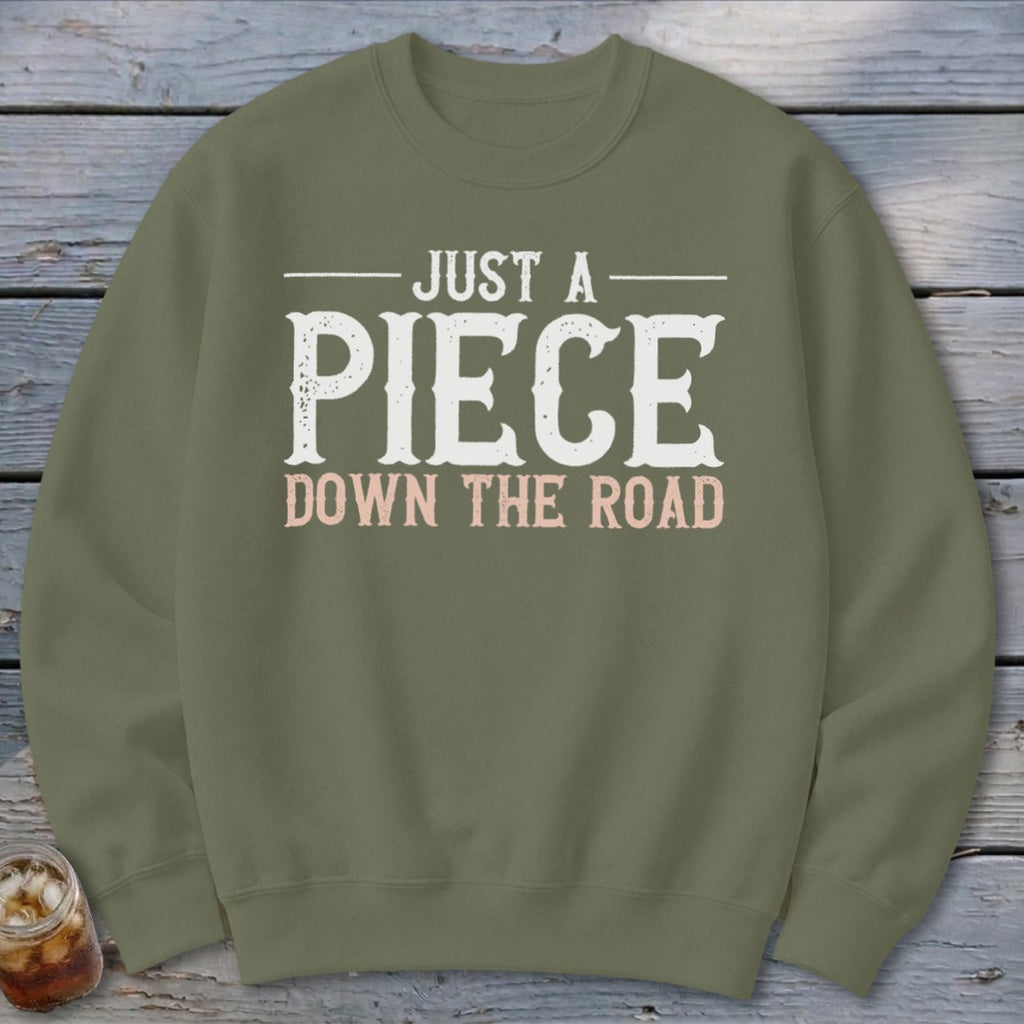 Olive green sweatshirt with white text "JUST A PIECE DOWN THE ROAD".