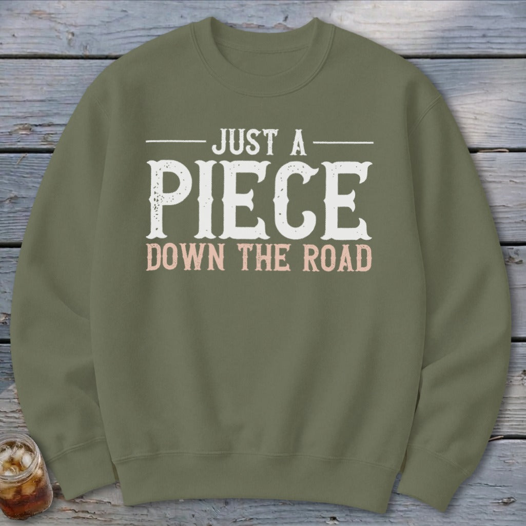 Olive green sweatshirt with white text "JUST A PIECE DOWN THE ROAD".