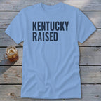 Light blue t-shirt with "KENTUCKY RAISED" printed in dark blue letters.