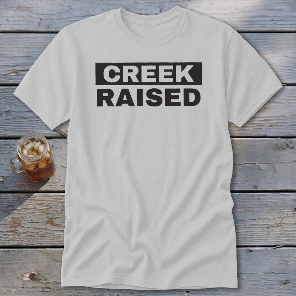 White t-shirt with black text that reads "CREEK RAISED" in a rectangular box.