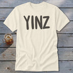 Cream t-shirt with dark gray "YINZ" text and a glass of iced tea.