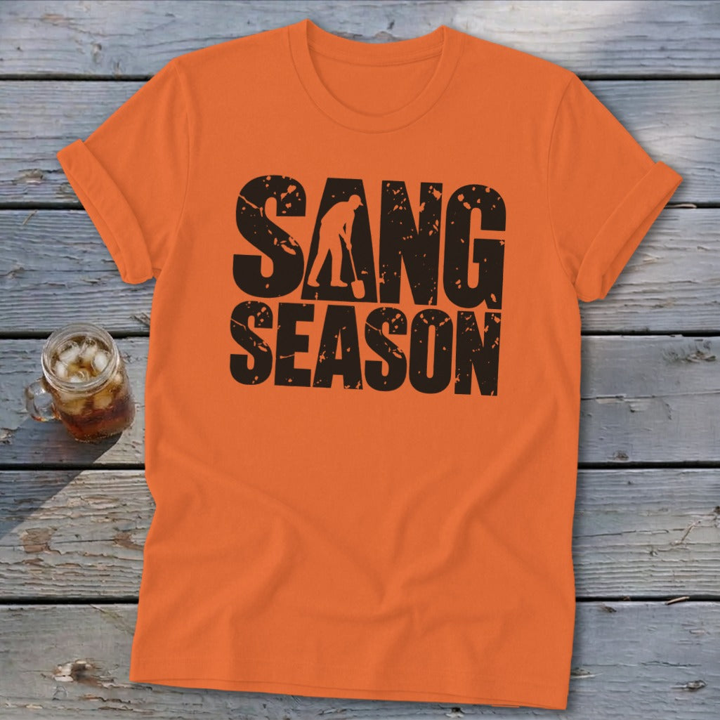 An orange t-shirt featuring distressed black text that reads SANG SEASON with a silhouette of a person digging.