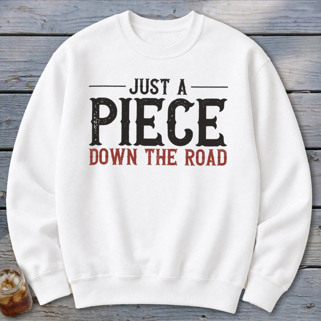 White crewneck sweatshirt with black text "JUST A PIECE" and red text "DOWN THE ROAD".
