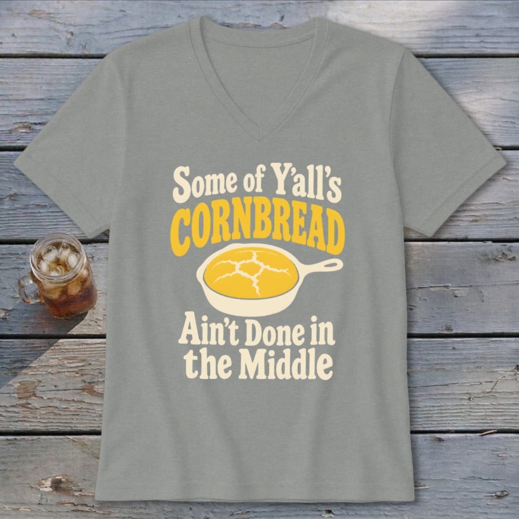 A grey V-neck t-shirt with a graphic of cornbread in a skillet and text reading Some of Yall s Cornbread Ain t Done in the Middle.