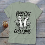 T-shirt with "Barefoot on the Creek Bank" text over bare feet on rocks in water.