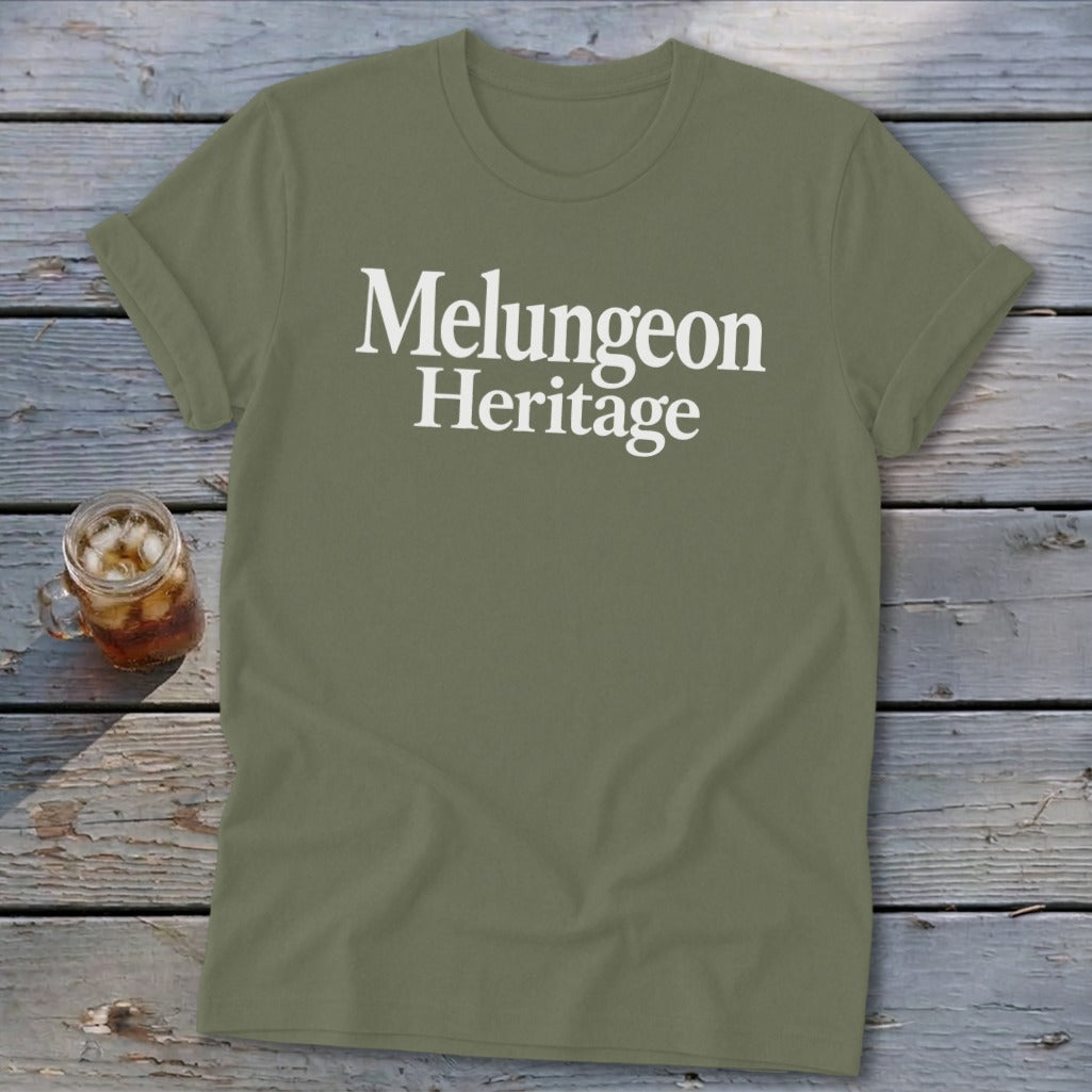 Olive green crewneck t-shirt featuring the white text Melungeon Heritage displayed centrally on a wooden surface with a small drink.