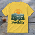 Yellow t-shirt with sun, mountains, trees, and "The Foothills" text.