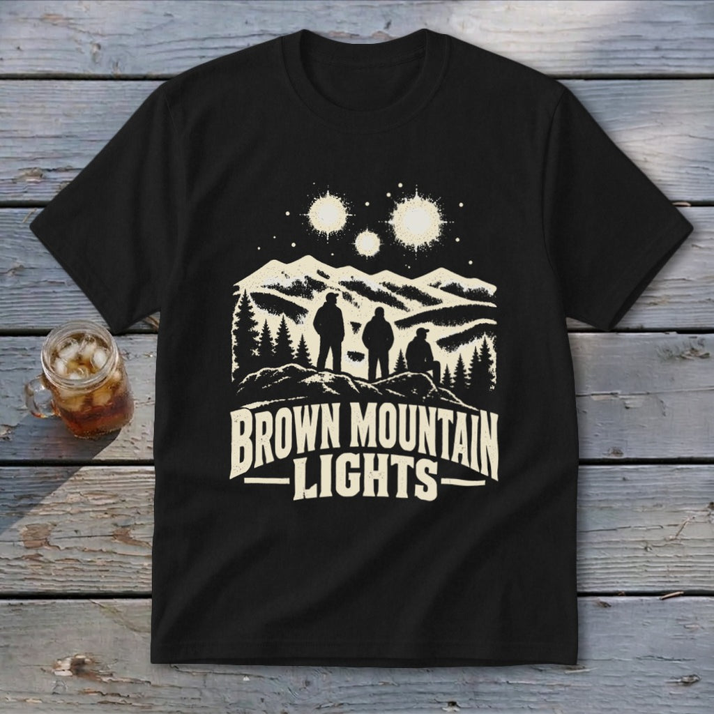 A black t-shirt features a graphic of three figures beneath glowing lights over mountains, with the text "BROWN MOUNTAIN LIGHTS".