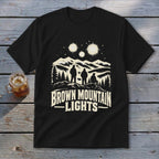 A black t-shirt features a graphic of three figures beneath glowing lights over mountains, with the text "BROWN MOUNTAIN LIGHTS".