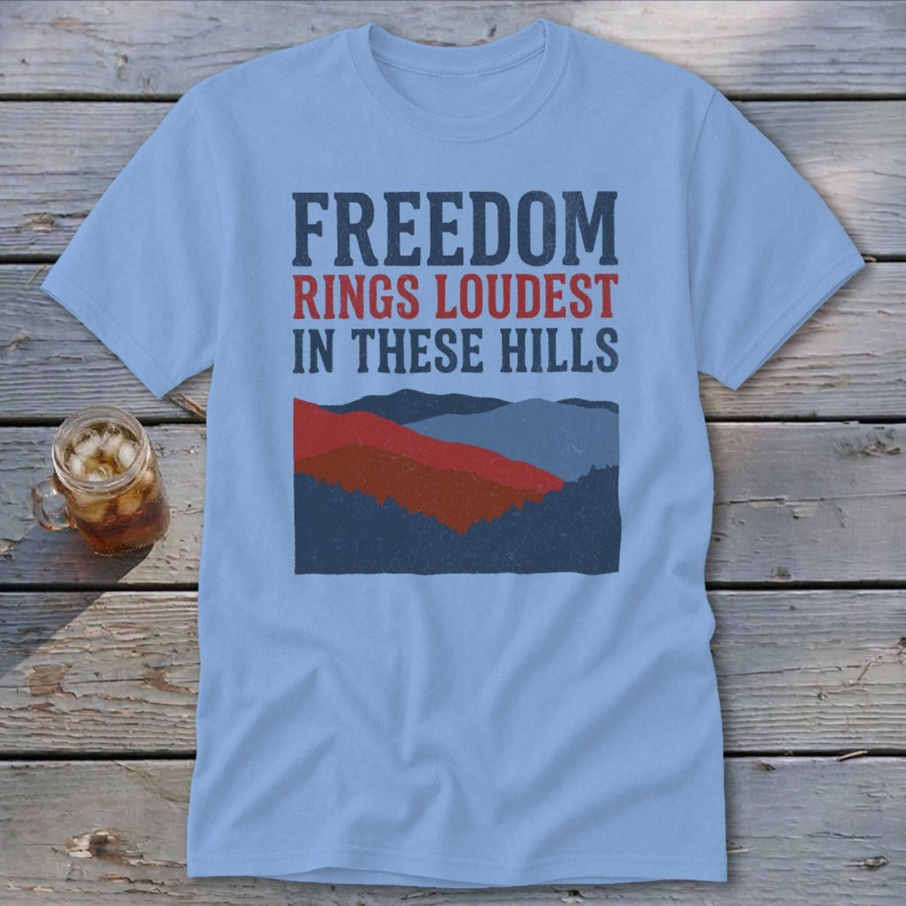 Light blue t-shirt featuring distressed text reading FREEDOM RINGS LOUDEST IN THESE HILLS above a mountain illustration.