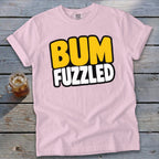 Light pink t-shirt featuring the text BUM FUZZLED on a wooden tabletop next to a drink.