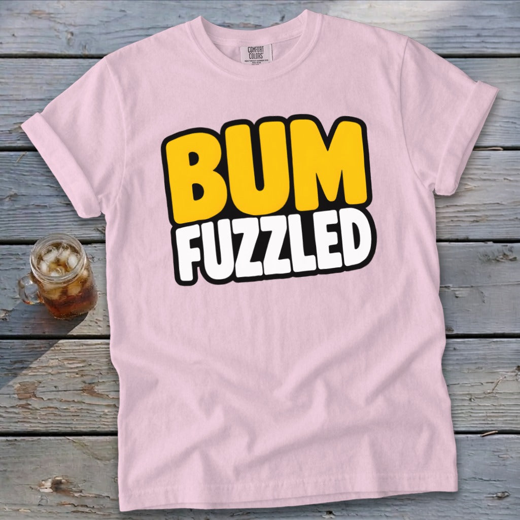 Light pink t-shirt featuring the text BUM FUZZLED on a wooden tabletop next to a drink.