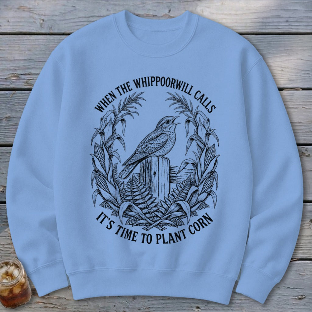 Light blue crewneck sweatshirt featuring a black graphic of a bird on a post surrounded by cornstalks and text.