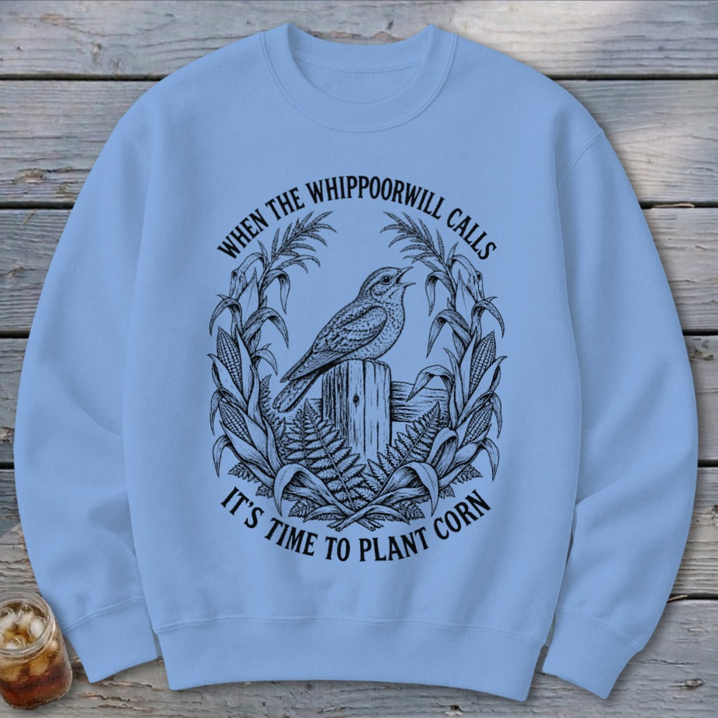 Light blue crewneck sweatshirt featuring a black graphic of a bird on a post surrounded by cornstalks and text.