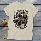 A cream-colored t-shirt displays a graphic of a bear relaxing in a rocking chair with a drink.