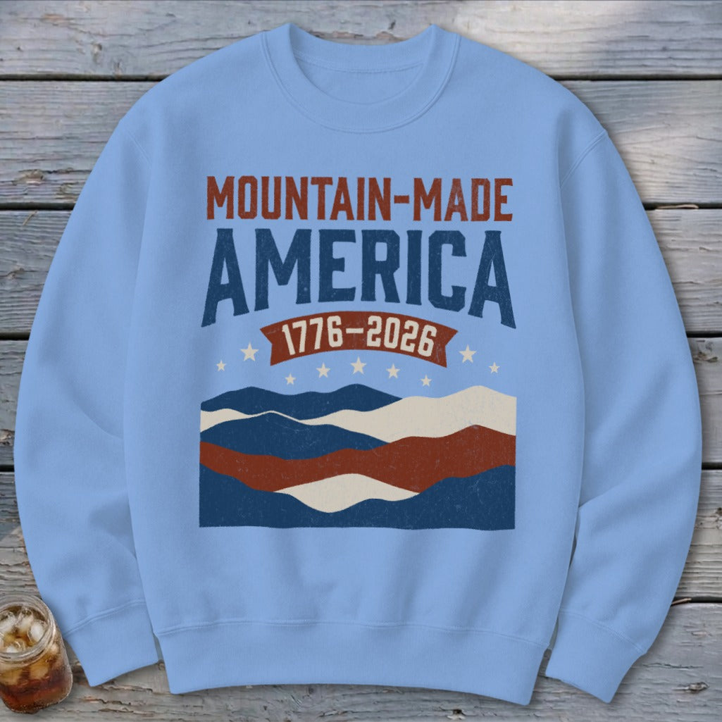 Light blue crewneck sweatshirt featuring a retro Mountain-Made America 1776-2026 design with wavy landscape stripes.