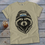 Tan t-shirt with a black graphic of a raccoon wearing a beanie with a mountain patch.