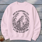 Light pink crewneck sweatshirt featuring a black vintage illustration of a bird on a fence post with the text "WHEN THE WHIPPOORWILL CALLS IT'S TIME TO PLANT CORN".