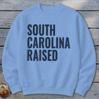 Light blue sweatshirt with "South Carolina Raised" text in dark blue.