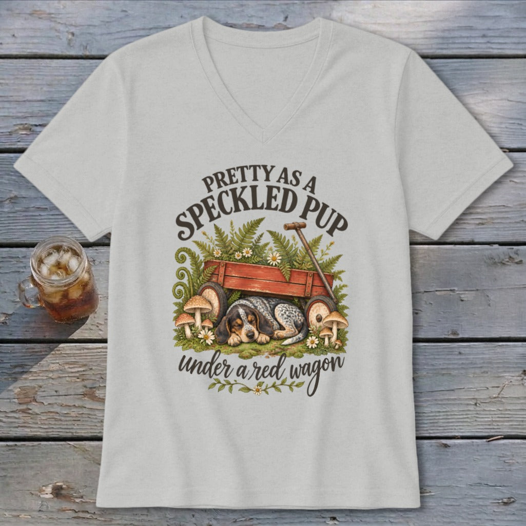 Speckled pup sleeps under a red wagon with mushrooms and ferns, "Pretty as a speckled pup under a red wagon."