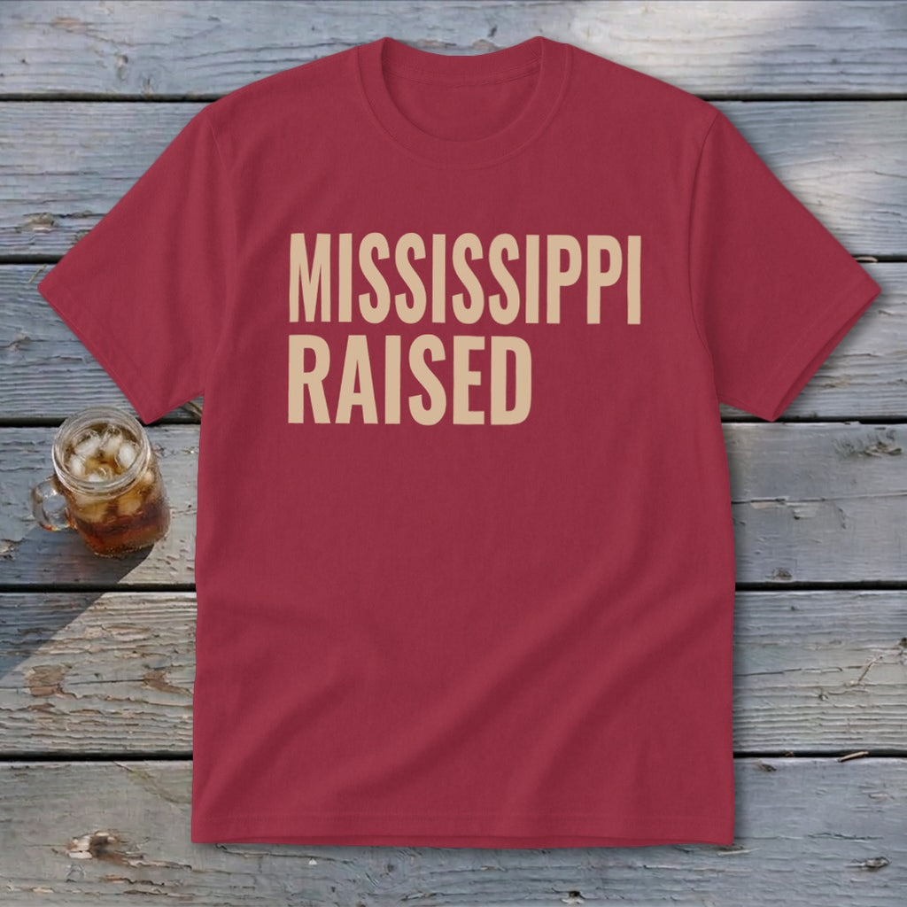 Maroon t-shirt with "MISSISSIPPI RAISED" text in tan, on wooden planks.