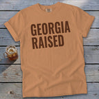 Orange t-shirt with "GEORGIA RAISED" printed in dark brown on the chest.