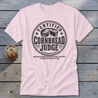 A light pink t-shirt featuring a black graphic with text reading "Certified Cornbread Judge".
