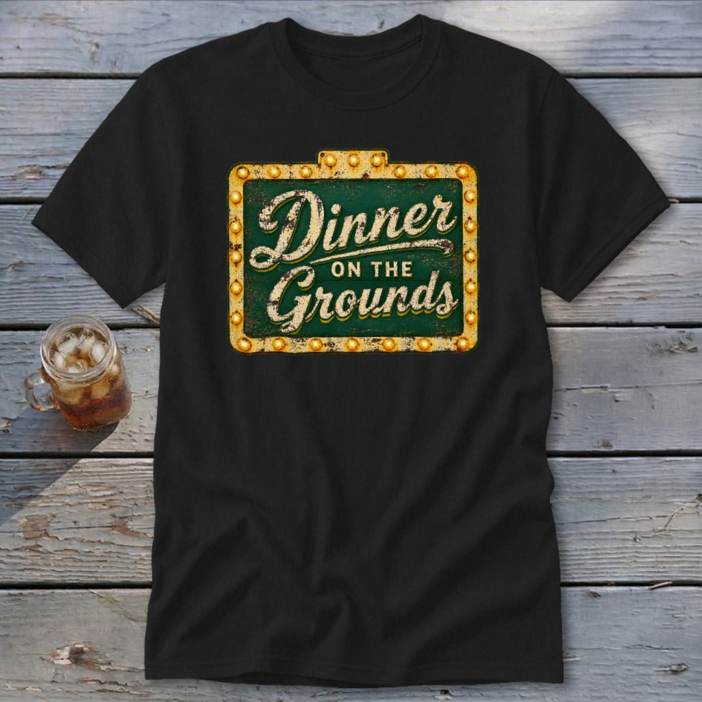A black short-sleeved t-shirt featuring a green vintage marquee graphic with the text Dinner on the Grounds.