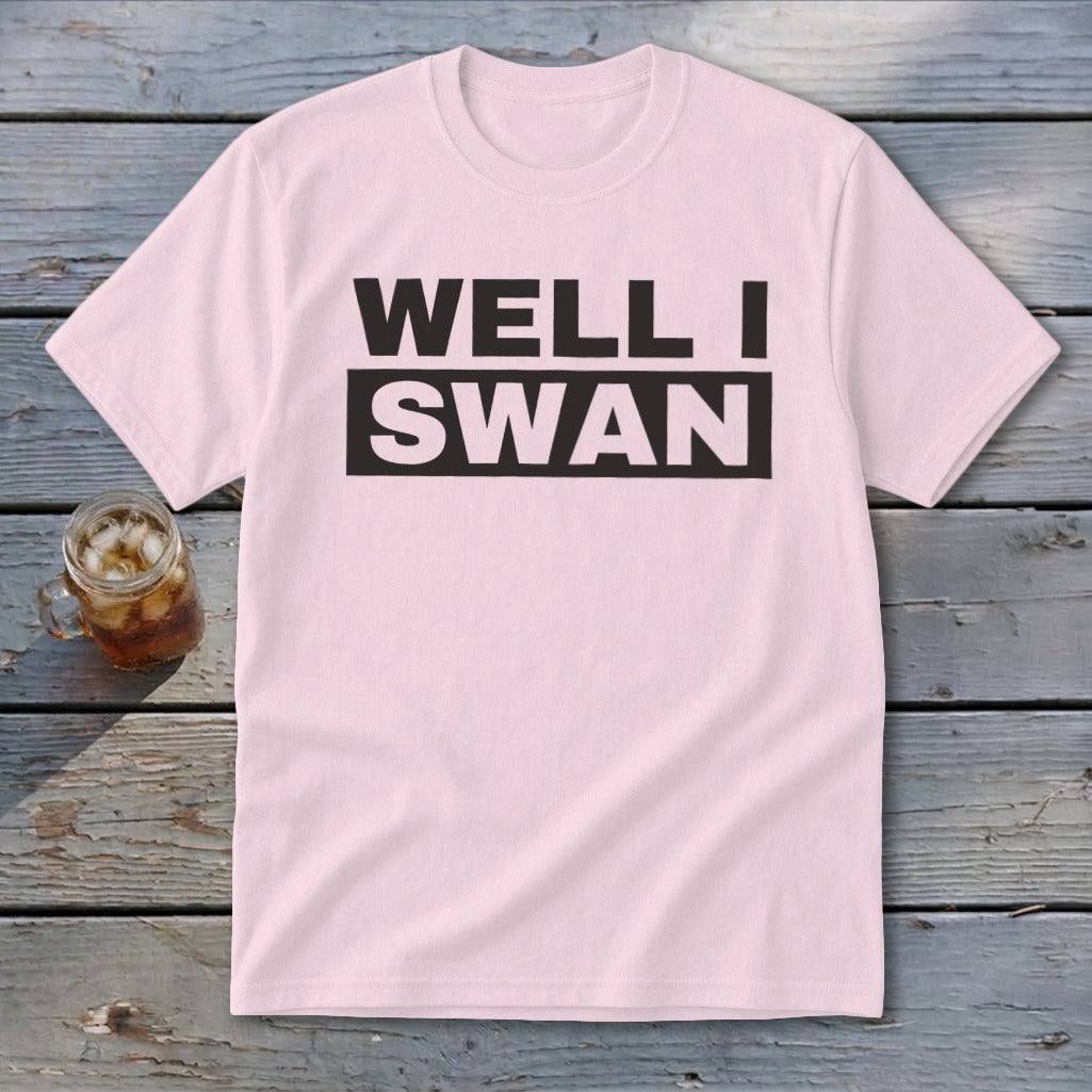 Light pink short-sleeve t-shirt with black block lettering reading WELL I SWAN laid on weathered wooden planks.