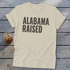 Cream t-shirt with "ALABAMA RAISED" in dark gray text.