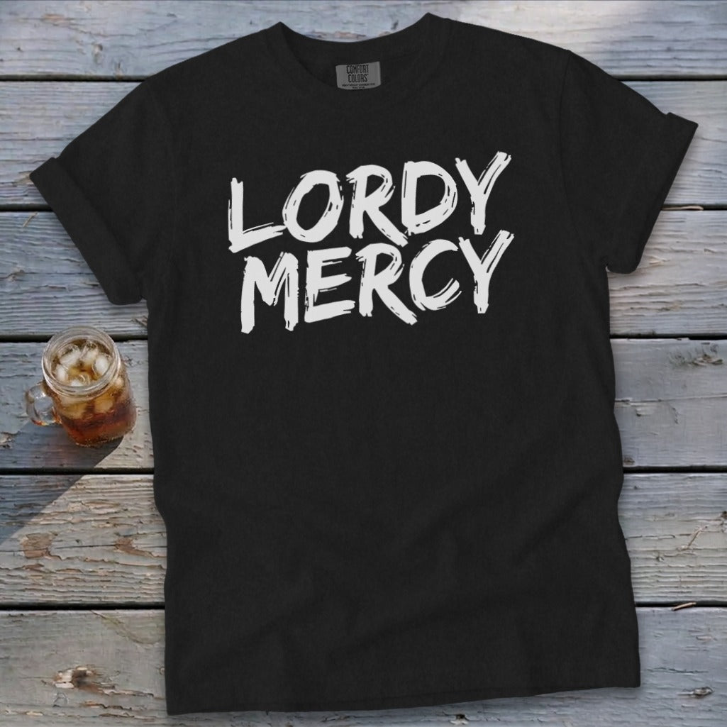 Black t-shirt with white text "LORDY MERCY" on a wooden background.
