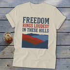 Beige t-shirt featuring the text "FREEDOM RINGS LOUDEST IN THESE HILLS" above a mountain graphic.