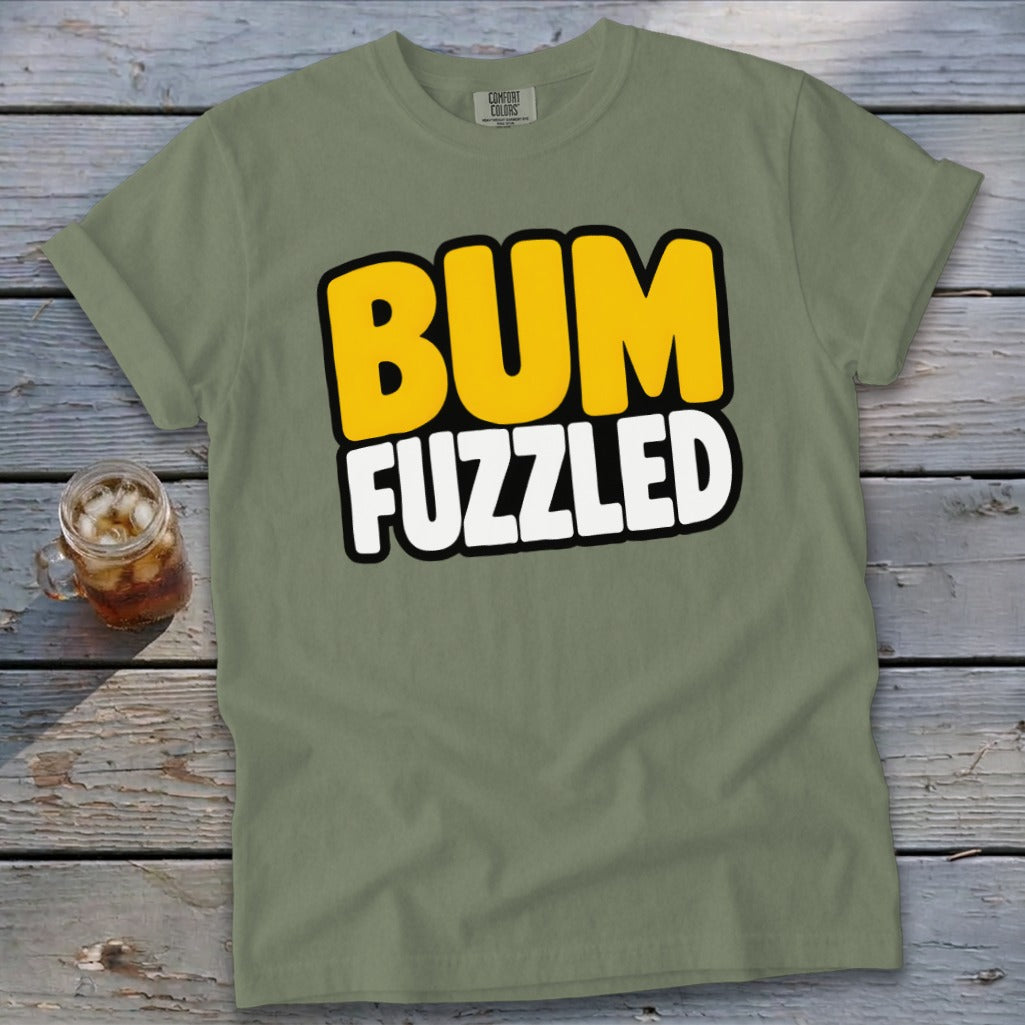 An olive green t-shirt with the text BUM FUZZLED on a wooden surface.