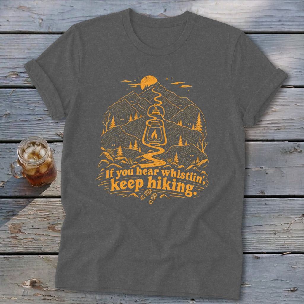 Dark gray t-shirt with orange graphic of mountains, lantern, and text "If you hear whistlin', keep hiking."
