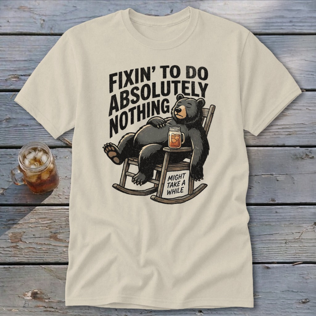 Cream t-shirt featuring a graphic of a bear lounging in a rocking chair with text reading "Fixin' to do absolutely nothing".