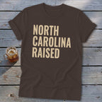 Brown t-shirt with "NORTH CAROLINA RAISED" text in cream.
