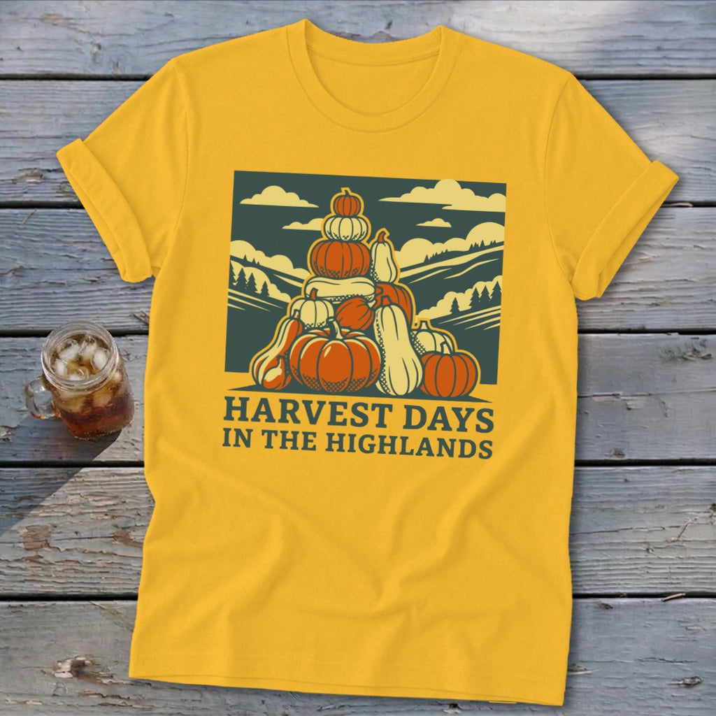 Golden yellow short-sleeve t-shirt featuring a graphic of stacked pumpkins, hills, and the text Harvest Days in the Highlands.