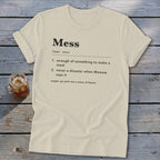 A cream crewneck t-shirt with a dictionary definition print of the word Mess lying on a wooden surface.