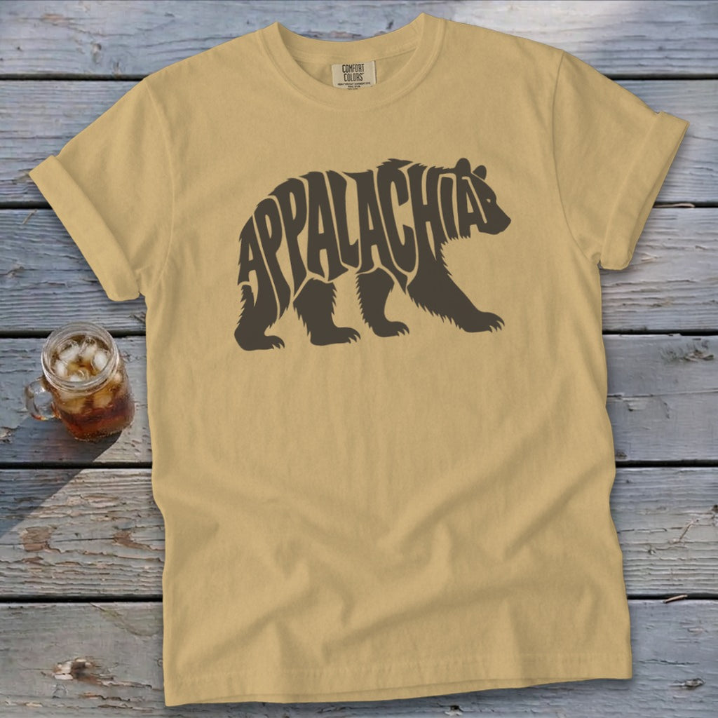 A tan t-shirt with a brown bear graphic containing the word Appalachia laid flat on a wooden surface.