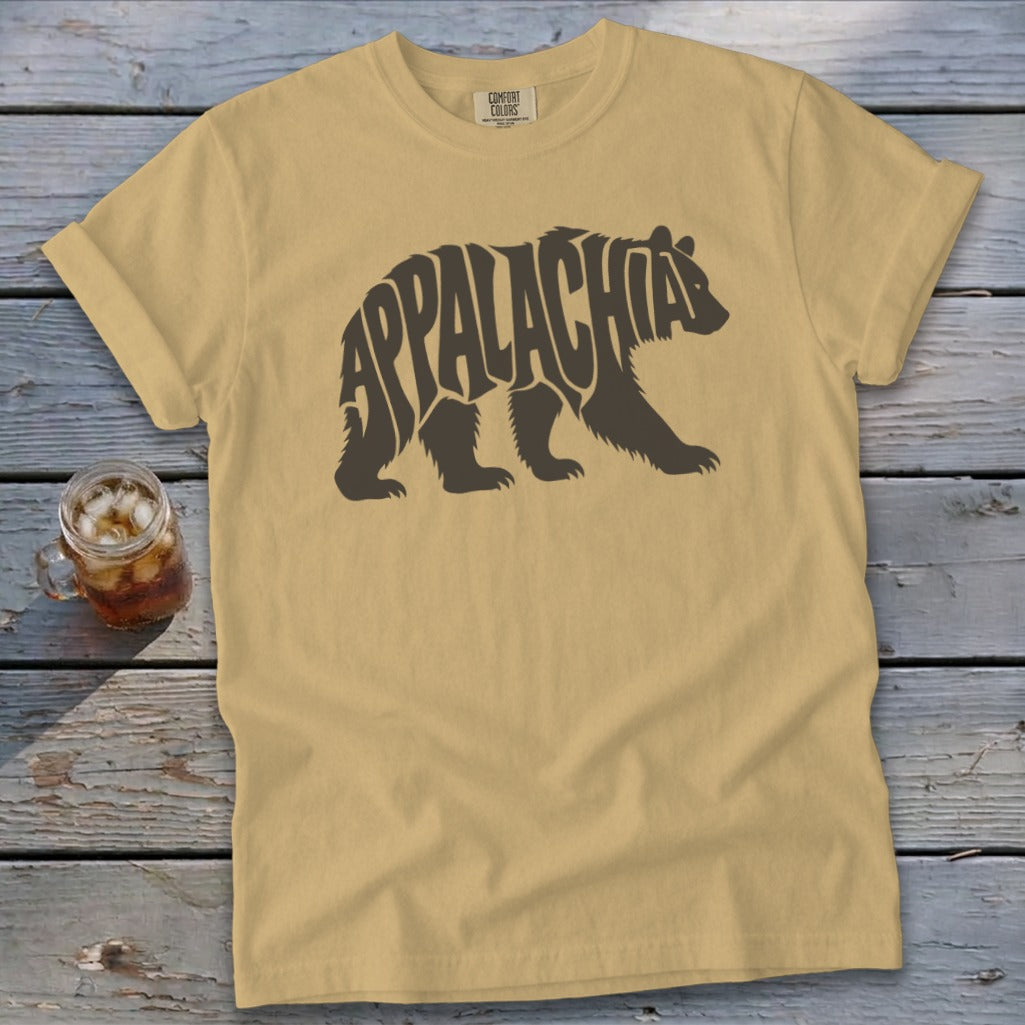 A tan t-shirt with a brown bear graphic containing the word Appalachia laid flat on a wooden surface.