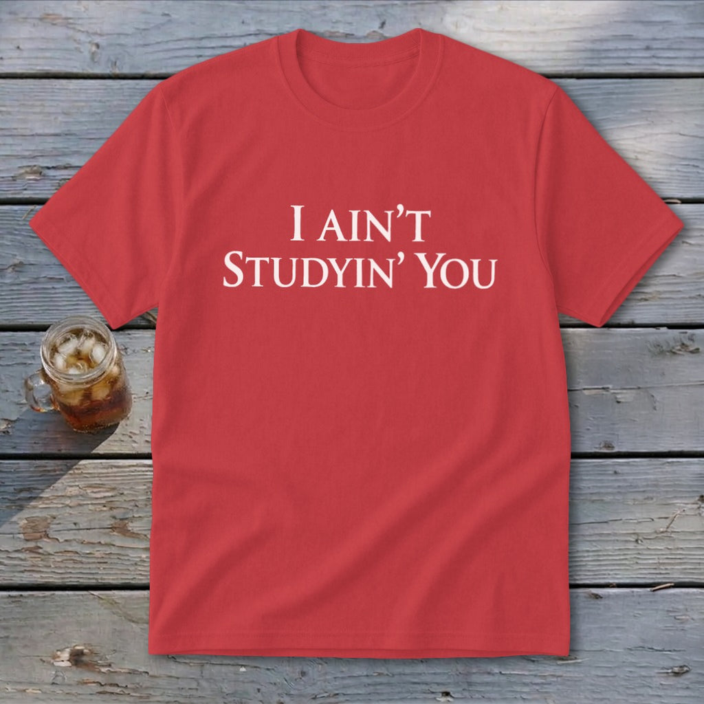 Red t-shirt with white text "I AIN'T STUDYIN' YOU" on a wooden background.