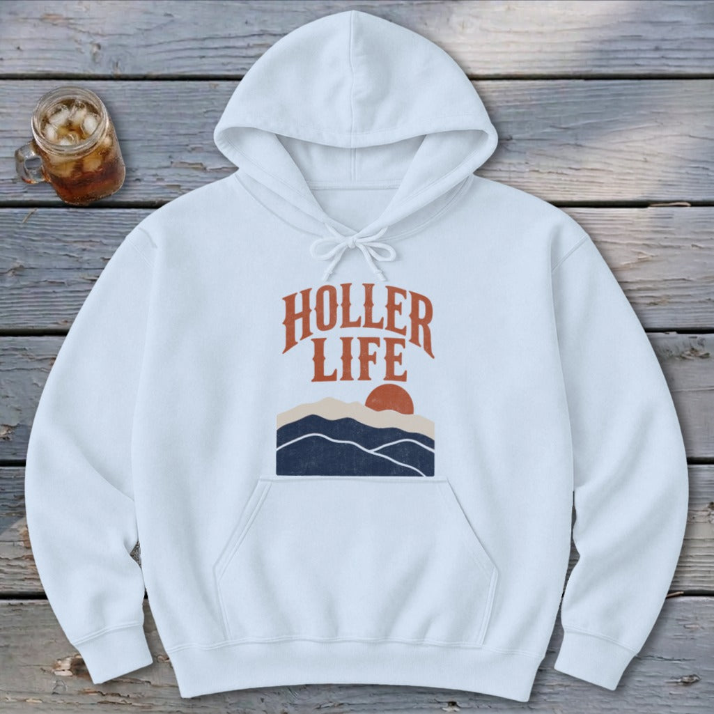 White hoodie featuring "HOLLER LIFE" text and a mountain sunset graphic on a wooden surface.