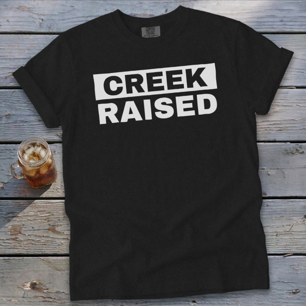Black Comfort Colors t-shirt with white text reading "CREEK RAISED".
