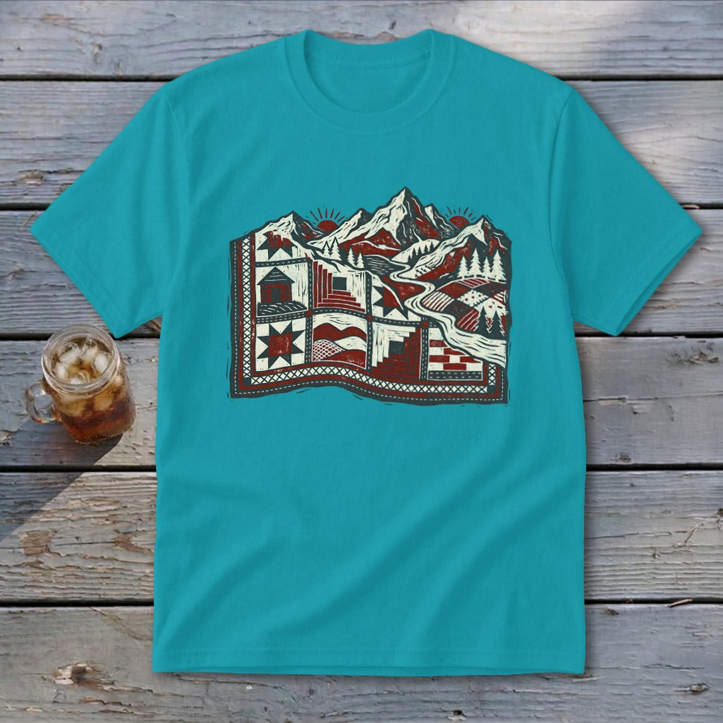 A turquoise short-sleeve t-shirt features a red and white graphic of a mountainous landscape integrated into a patchwork quilt.