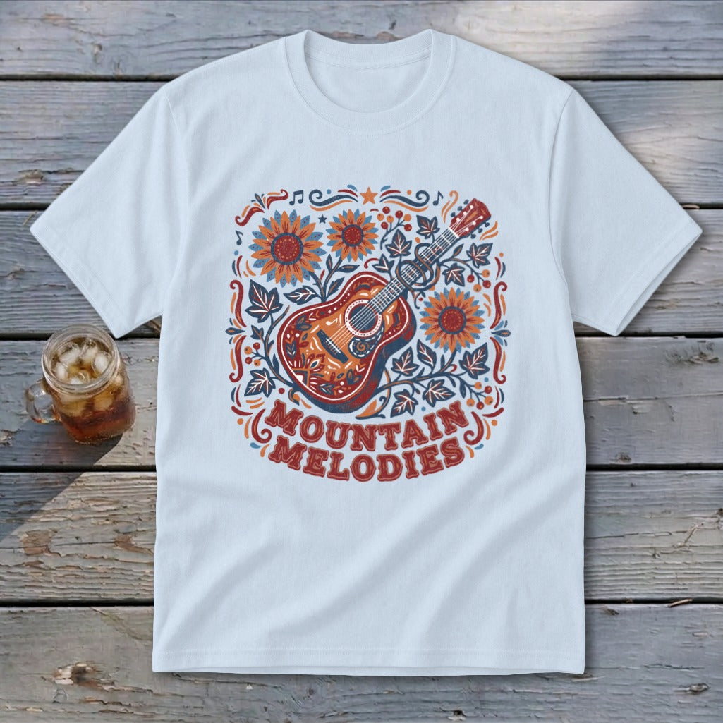 A white t-shirt featuring a colorful graphic of an acoustic guitar, sunflowers, and the text MOUNTAIN MELODIES.