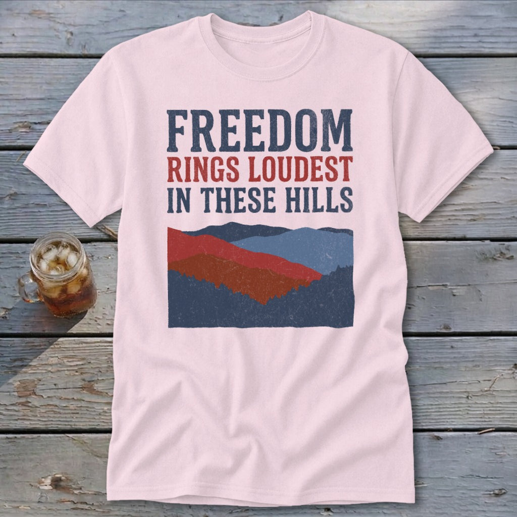 A pink crewneck t-shirt featuring a mountain graphic and the text FREEDOM RINGS LOUDEST IN THESE HILLS.