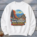 White sweatshirt with autumn mountain road graphic and text "Peak weekend. Same playlist. New overlook."